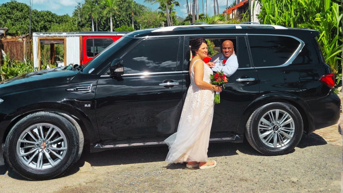 Bride and groom standing next to a black SUV in a tropical setting